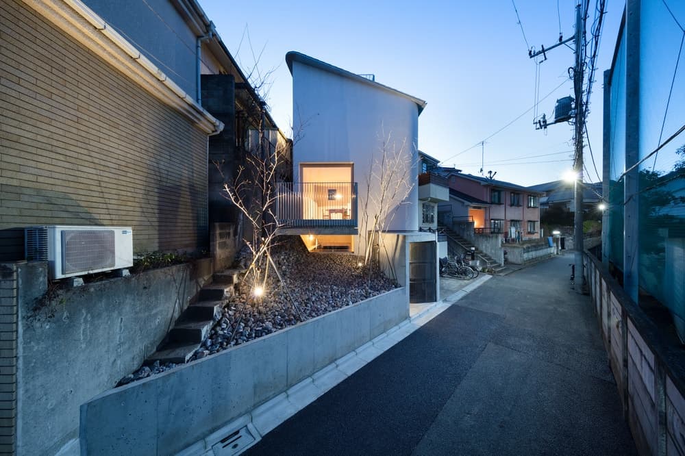 This is a view of the house from the vantage of the street showcasing its unique triangular design and the large balcony on the side of the house over a rocky landscape.