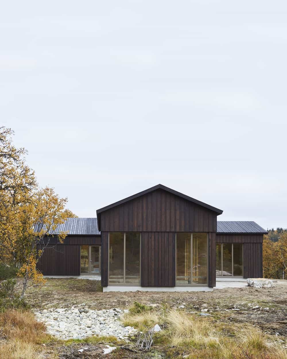 This is a view of the back of the house that has a consistent dark wooden exterior tone to the walls that pair well with the glass walls and doors.