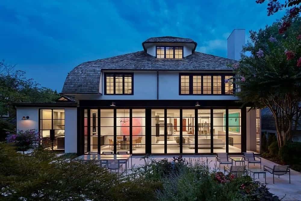 The house has an abundant amount of glass walls and windows that have frames and grids to create a unique look that glows at night from the warmth of the interior lights.