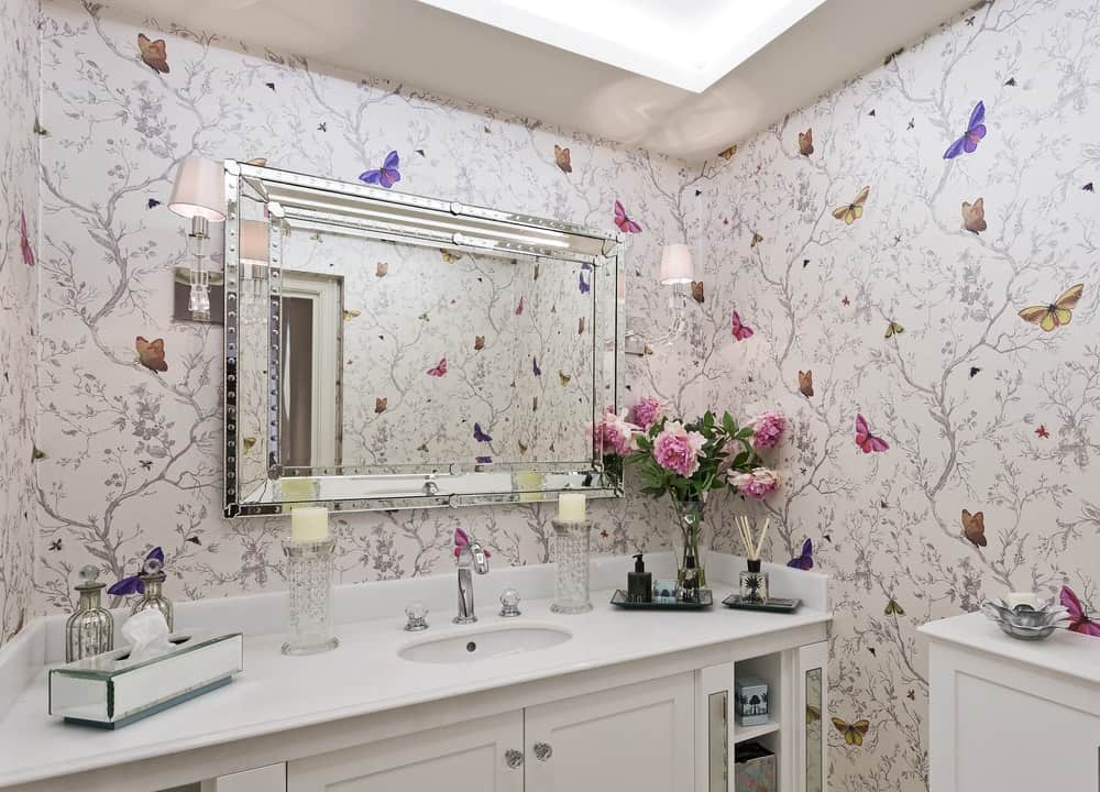 A bathroom vanity area complemented by the ornate wallpaper full of butterflies.