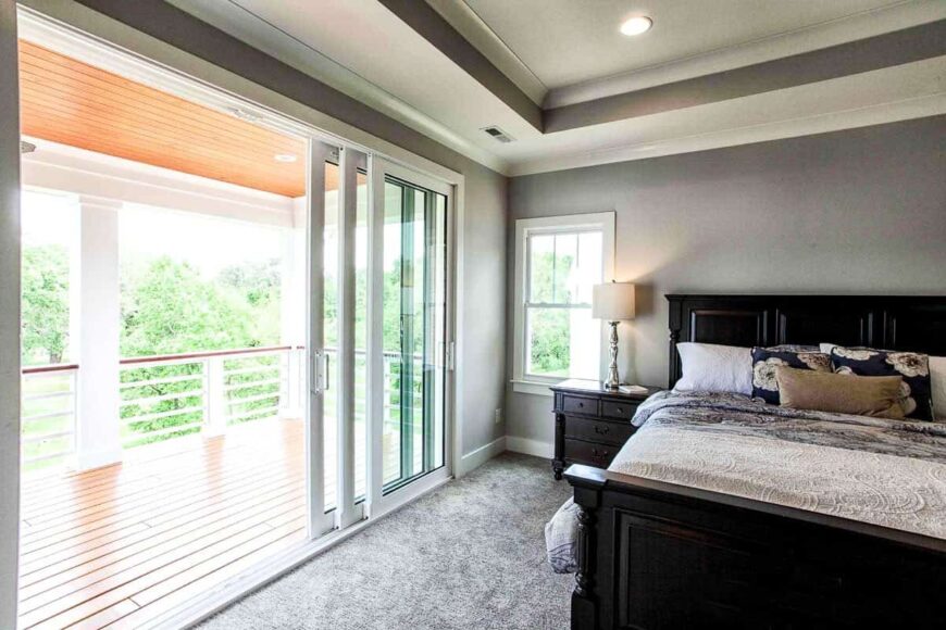 The primary bedroom has gray walls, carpet flooring, tray ceiling and sliding glass doors that lead out to the covered porch.