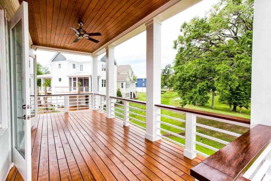 The covered porch has a rich hardwood flooring that matches the paneled ceiling mounted with a fan.