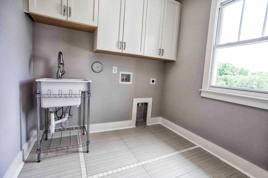 Laundry room with white cabinets, a washstand, and a framed window that brings natural light in.