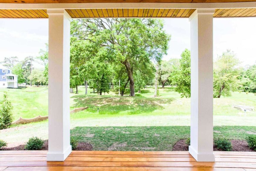 View of the serene lush backyard from the covered porch supported by sleek white columns.