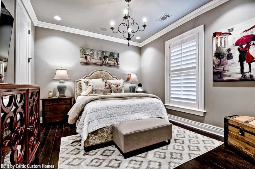 This bedroom has wide plank flooring and gray walls adorned by lovely paintings.