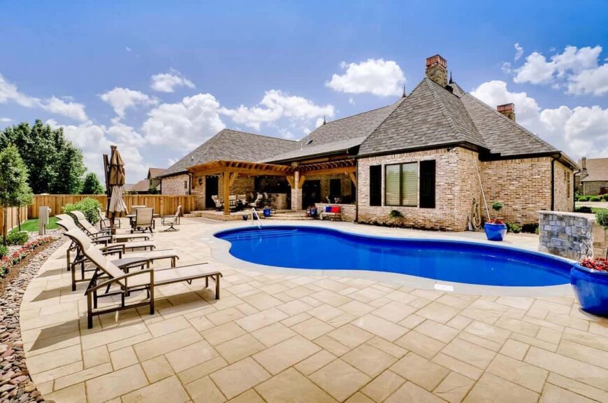 Home's rear exterior view showing the outdoor living and a freeform pool with tiled paving.