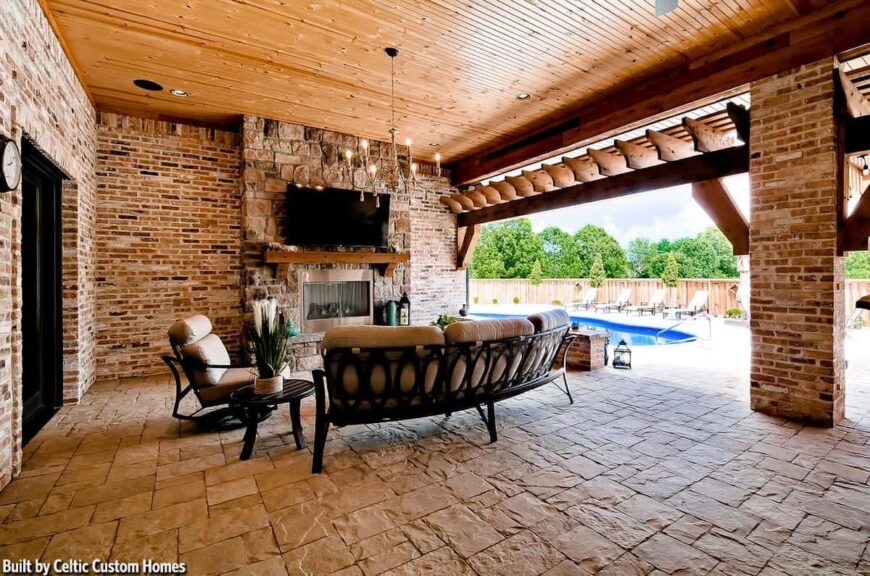 Outdoor living with cushioned seats and a glass-enclosed fireplace under the wall-mounted TV.