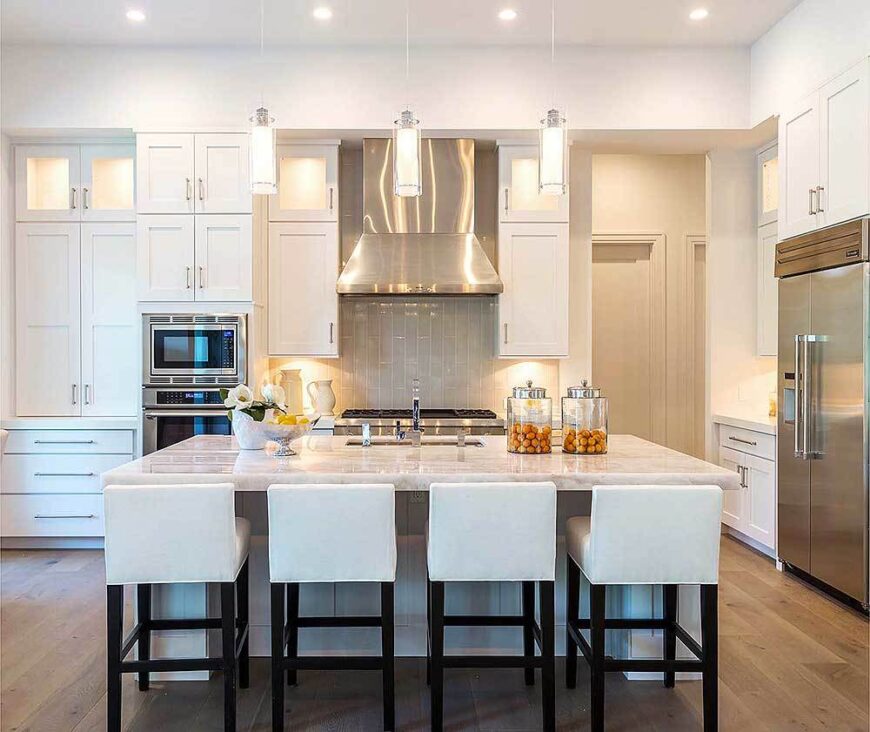 The kitchen is equipped with stainless steel appliances, white cabinetry, and an undermount sink fitted on the marble top island.