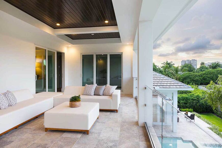 Covered balcony with sleek white sofas and a matching ottoman over limestone flooring.