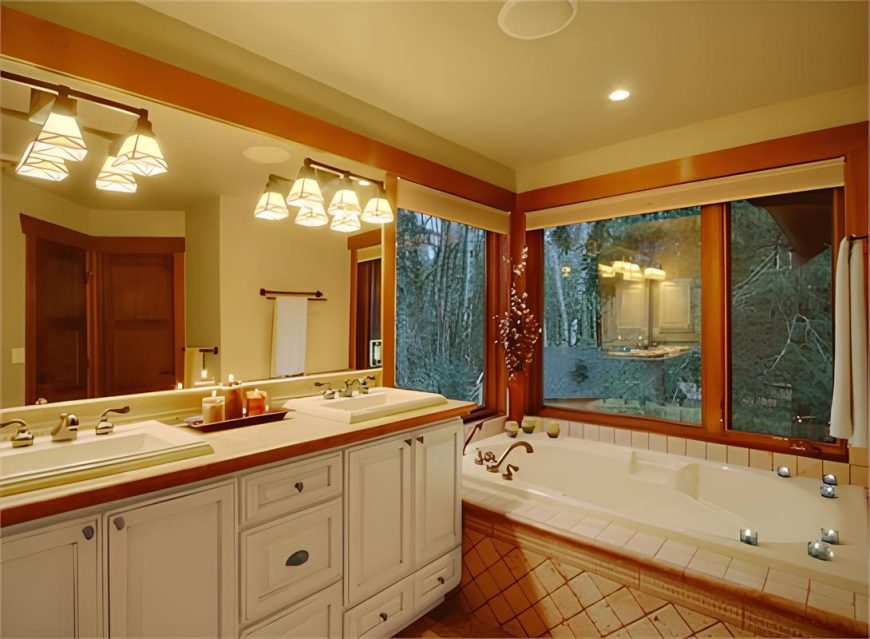 Primary bathroom with a deep soaking tub and a dual sink vanity placed under the frameless mirror and glass sconces.