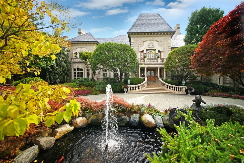 This is an aerial view of the front of the house that is complemented by the surrounding landscape of tall trees, colorful shrubs and a pond with a fountain across from the large courtyard of the main entrance. Image courtesy of Toptenrealestatedeals.com.