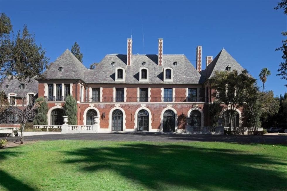 This is a look at the front of the house with red brick exteriors, dormer windows, arches on the ground floor and tall chimneys. Image courtesy of Toptenrealestatedeals.com.