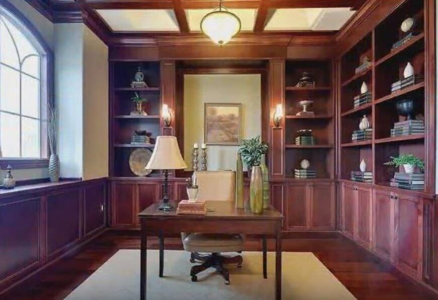 Study with a wooden desk, leather swivel chair, coffered ceiling, and built-in bookcases that blend in with the hardwood flooring.