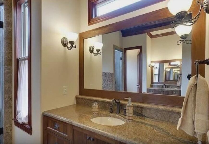 Powder room with granite top vanity and a large framed mirror illuminated by iron sconces.