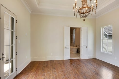 Primary suite with hardwood flooring and a tray ceiling mounted with a beaded chandelier.