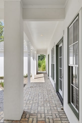 Covered porch with brick flooring and large columns that blend with the white ceiling.