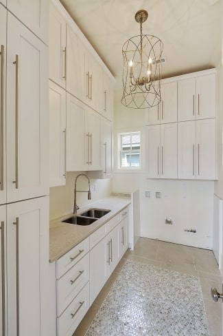 The utility room is filled with white modular cabinets, a double bowl sink, and a cylindrical chandelier.