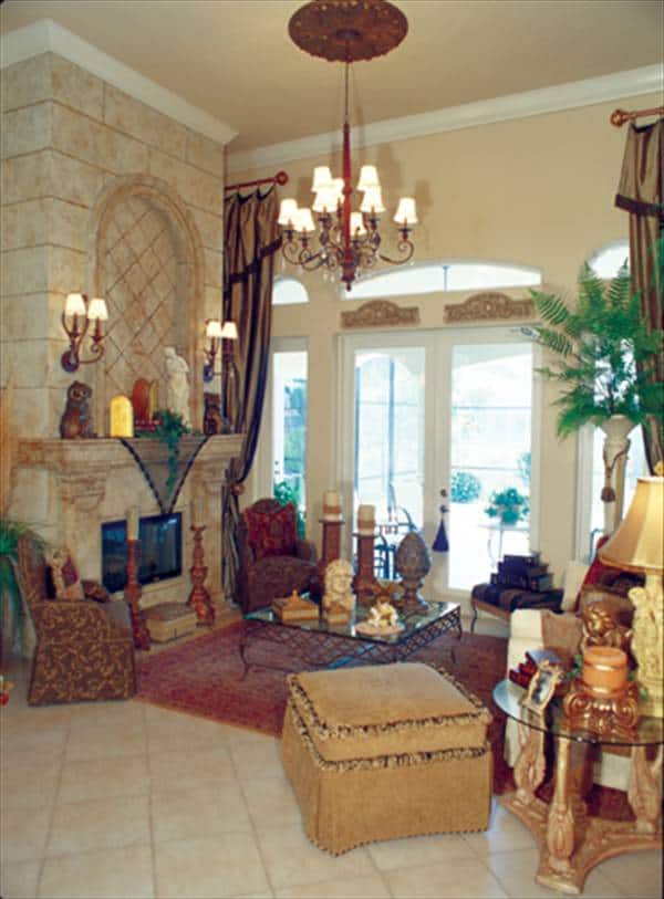 The living room has classy patterned seats, a glass top coffee table, a marble fireplace, and an ornate chandelier.