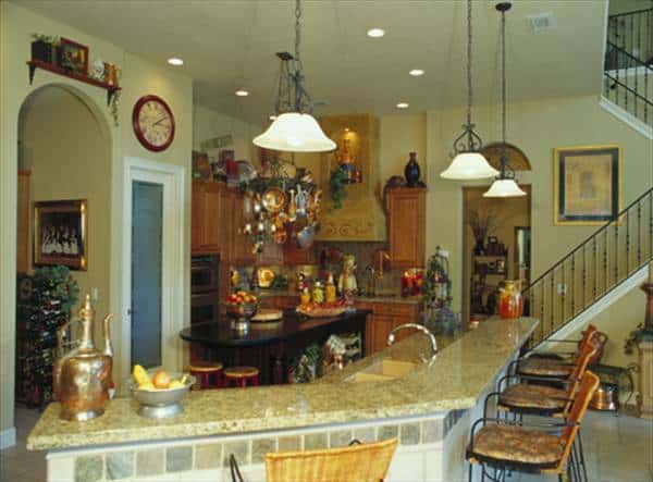 The kitchen is equipped with a two-tier island bar, wooden cabinetry, granite countertops, and glass dome pendants.