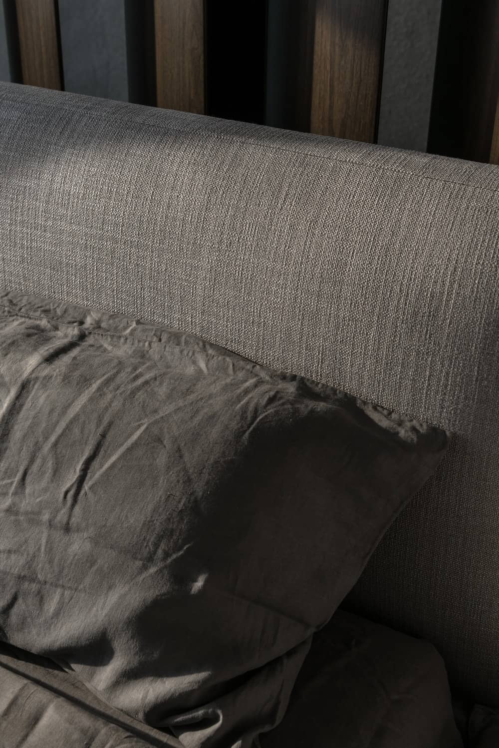 This is a close look at the gray cushioned headboard of the bed paired with matching gray pillows.