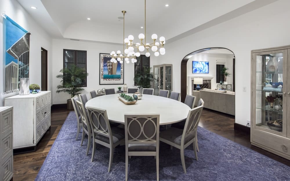 This is the formal dining room with a large white circular dining table surrounded by gray dining chairs and topped with round chandeliers. These are then complemented by the area rug on the dark hardwood flooring underneath. Image courtesy of Toptenrealestatedeals.com.