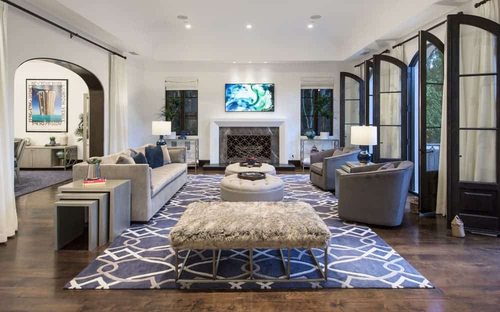 This is the family room with a sofa, a couple of cushioned armchairs and a couple of tufted ottomans for coffee table that stand out against the gray area rug. Image courtesy of Toptenrealestatedeals.com.