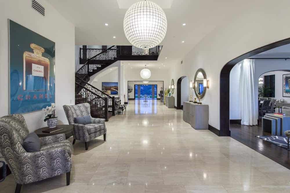 Upon entry of the mansion, you are welcomed by this foyer with marble floors, a large spherical pendant light, a couple of cushioned armchairs and a large painting on the wall. Image courtesy of Toptenrealestatedeals.com.