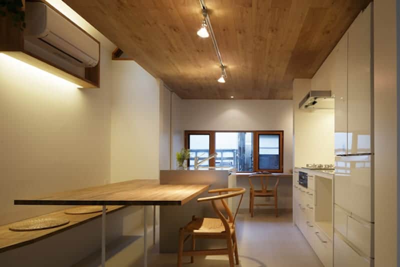 The eat-in kitchen is topped with a wooden ceiling that supports modern lighting and spotlights that illuminated the kitchen along with the window on the far side.