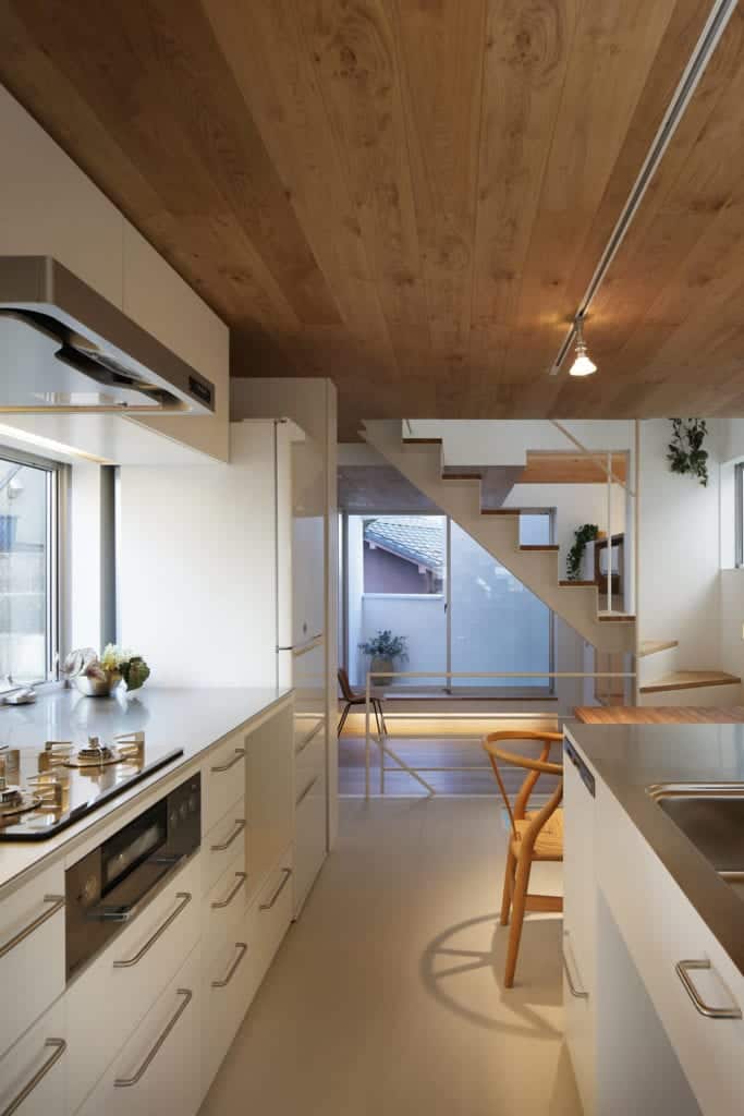 Across from the built-in wooden dining table of the kitchen is the cooking area surrounded by white cabinetry and a modern vent above.