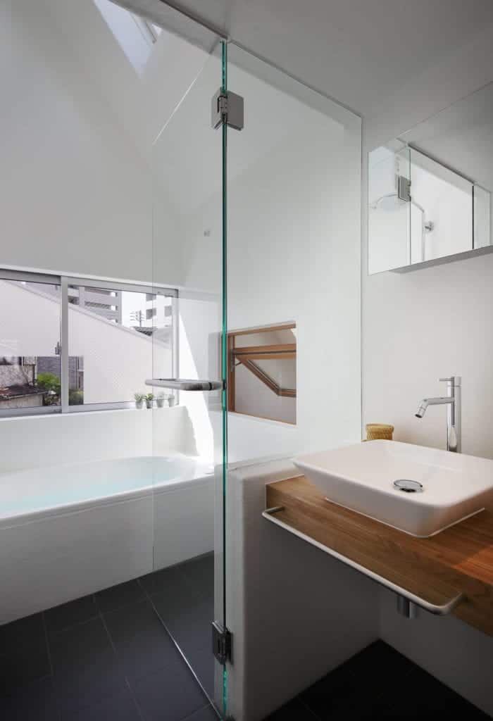 The modern bathroom has a bathtub and a floating sink that is separated with a half-wall of glass.