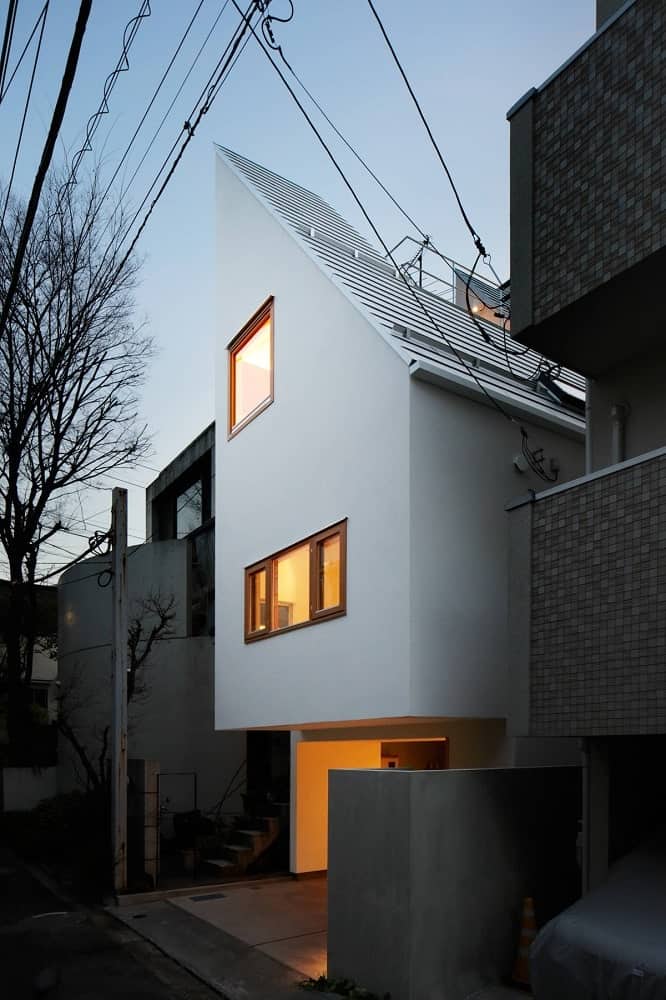 This nighttime view of the house features the warm glow of the windows that match the car port area complementing the bright exteriors.