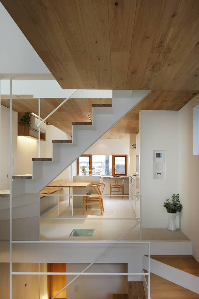 At the far side after the staircase, you can see the kitchen with a built-in wooden dining table on its kitchen island.