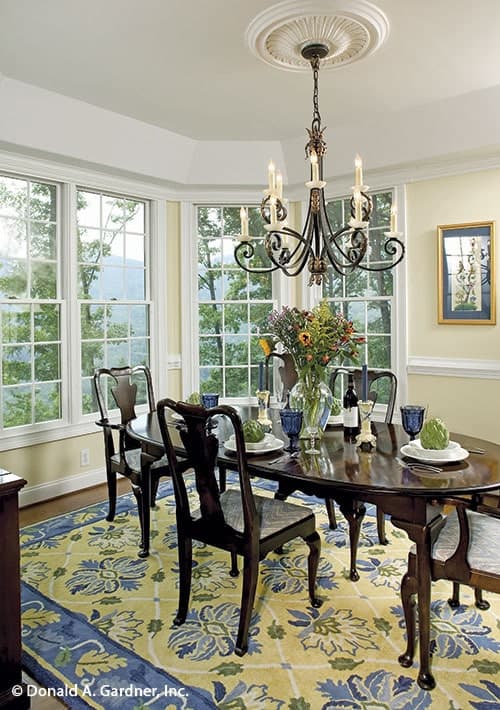 The dining area has a large floral rug, cushioned chairs, an oval dining table, an ornate chandelier, and a bay window.The dining area has a large floral rug, cushioned chairs, an oval dining table, an ornate chandelier, and a bay window.