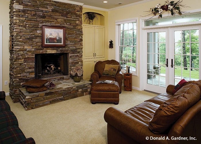 Recreation room with a stone fireplace, leather seats, white built-ins, and a french door that leads out to the rear patio.