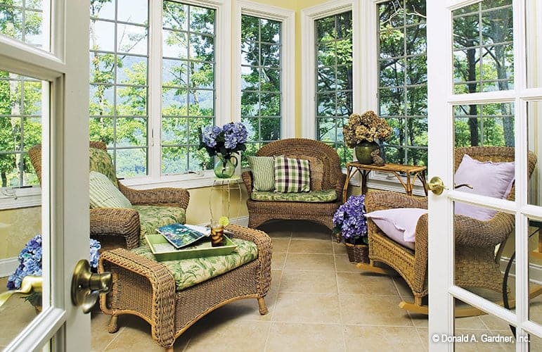 The sunroom is filled with wicker seats, wooden tables, and decorative flower pots.