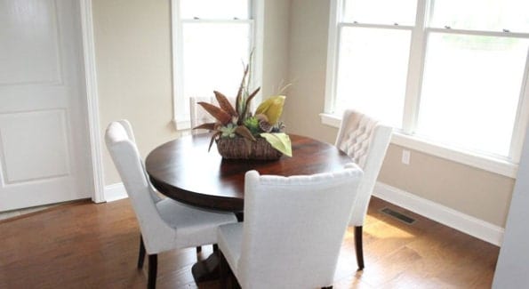 The dining area has tufted wingback chairs and a round wooden table topped with a potted plant.