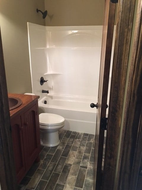 This bathroom has a wooden vanity, a toilet, and a tub and shower combo.