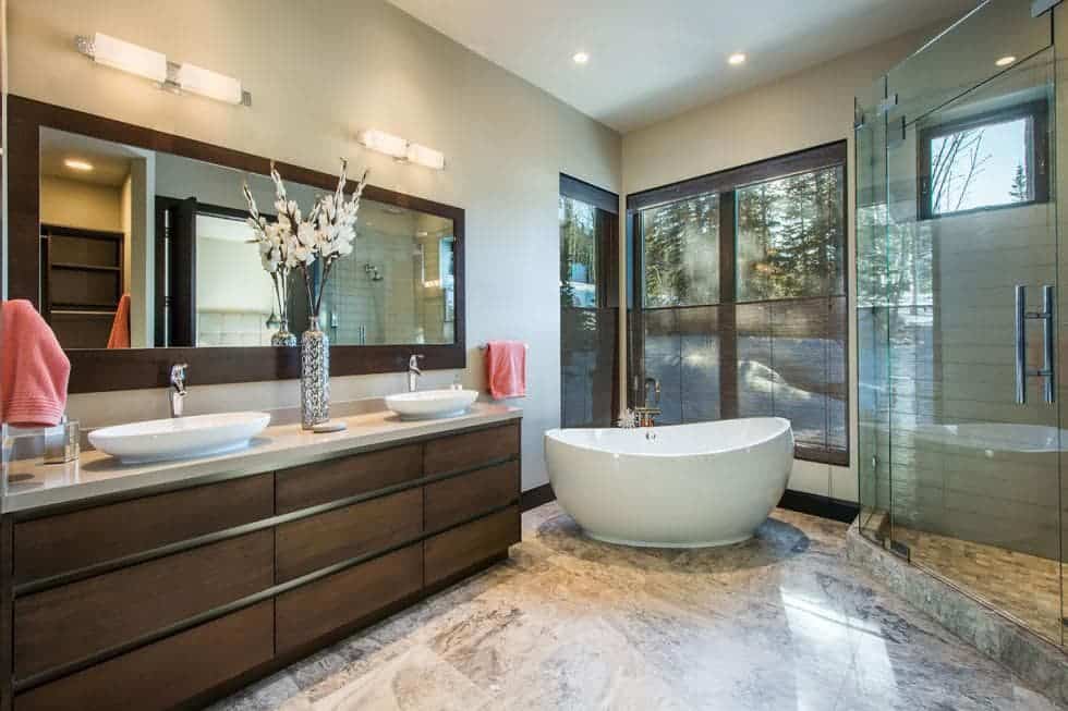 This is the spacious bathroom with a freestanding white bathtub placed at the far corner by the glass wall beside the dark brown vanity and glass-enclosed shower area. Image courtesy of Toptenrealestatedeals.com.