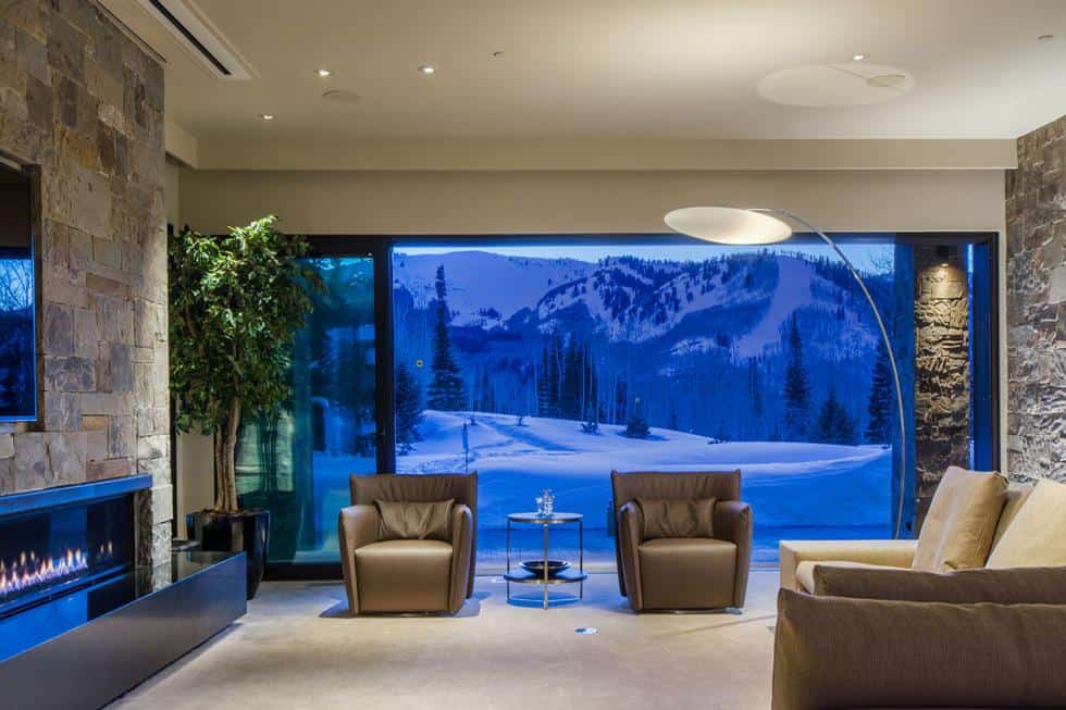 This is the living room on the ground floor with comfortable armchairs and sofa across from the wall-mounted TV above the fireplace. These are then complemented by the large glass wall. Image courtesy of Toptenrealestatedeals.com.