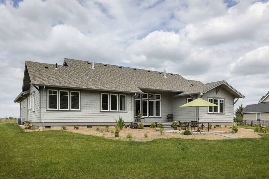 Rear exterior view showing the cedar shake siding, white-framed windows, and a sleek porch that leads to an open patio.