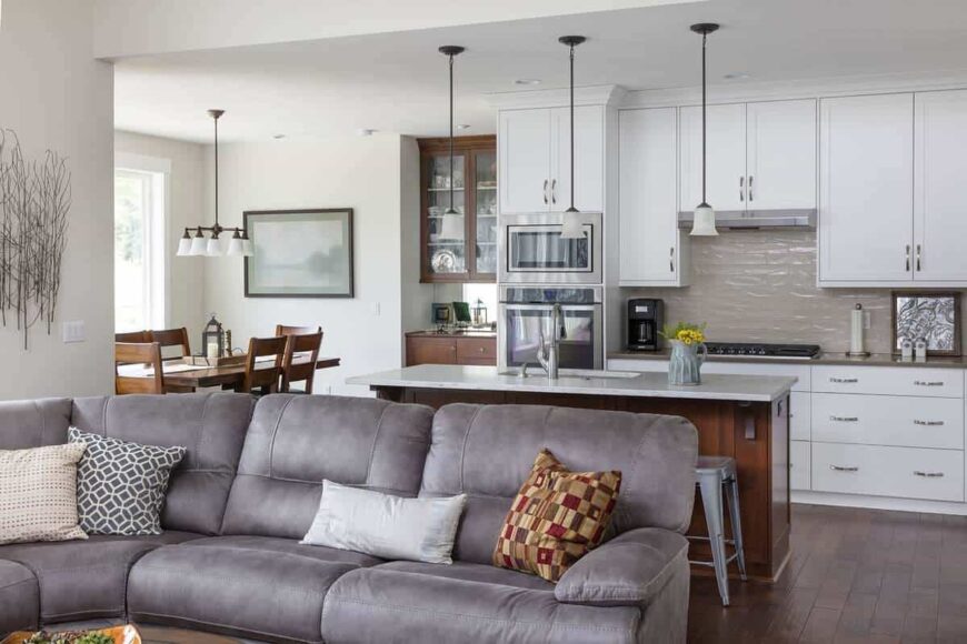 Behind the sofa is the eat-in kitchen with white cabinetry, stainless steel appliances, a center island, and a wooden dining set.