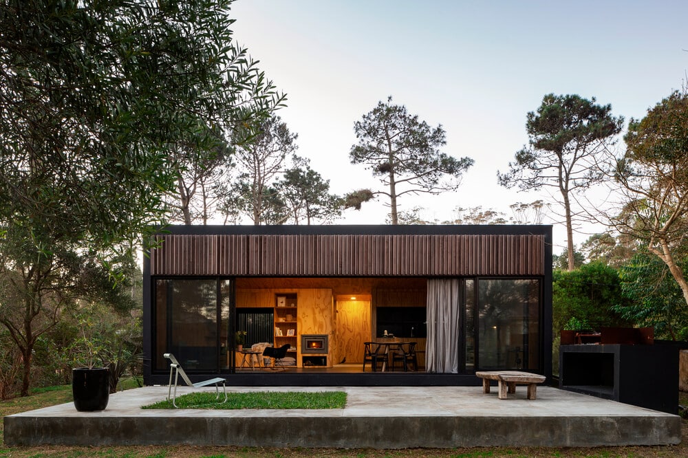 This home has dark brown slatted exterior walls that pair well with the warm interiors that escape through the large opening.