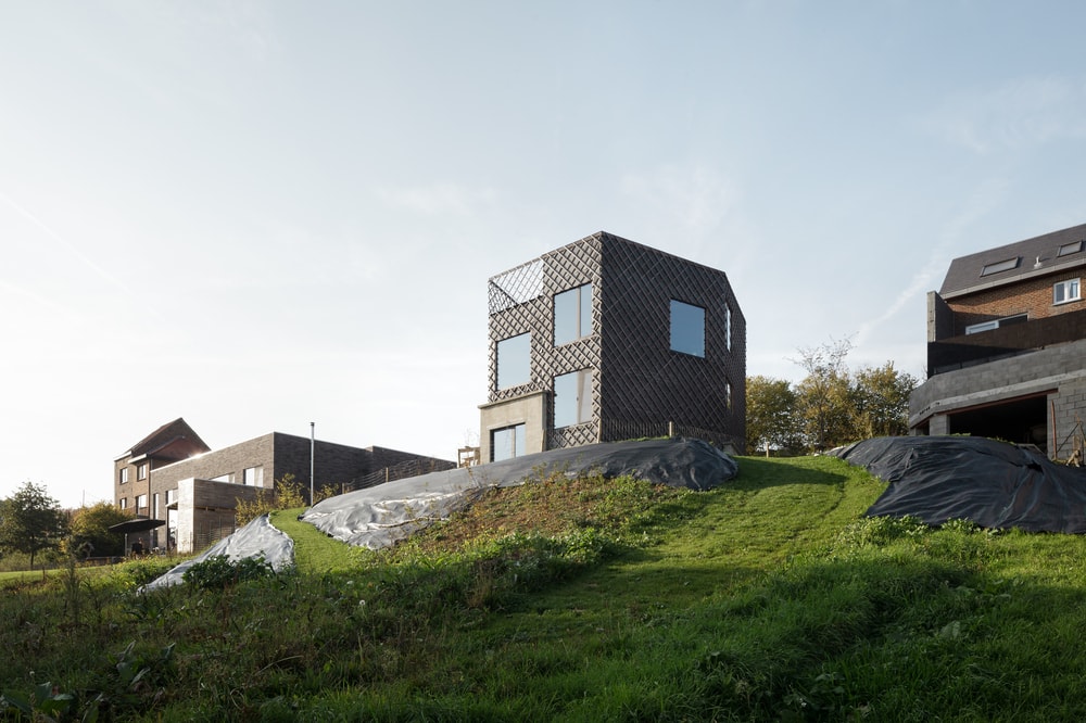 This is a view of the house on top of the hill with a patterned and textured dark gray exterior walls that make the glass walls stand out.