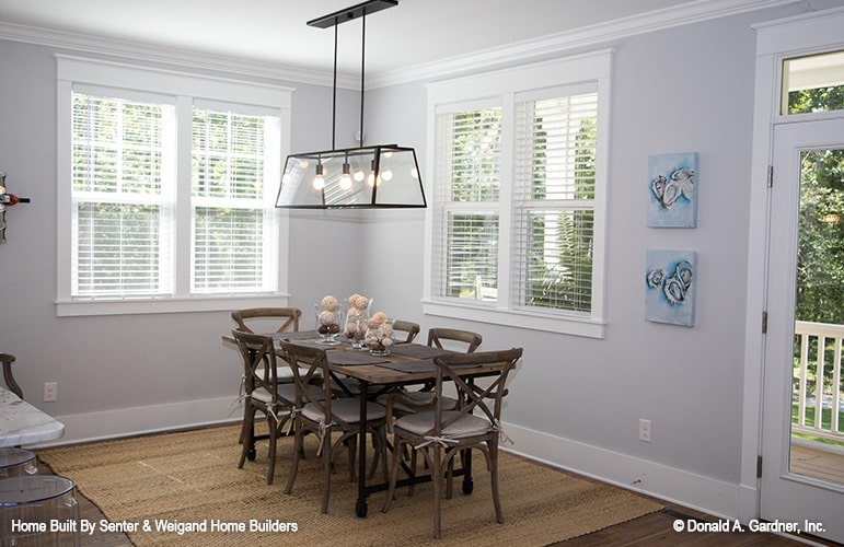 Dining area with a wooden dining set, wrought iron pendant light, and white framed windows.