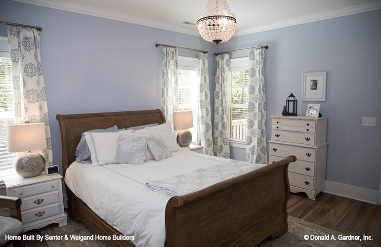 The primary bedroom has a cozy wooden bed, white cabinets, light blue walls, and a crystal chandelier.