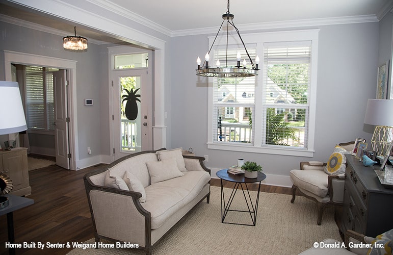 Sitting room with beige seats, dark wood tables, and round chandelier, and a jute area rug.