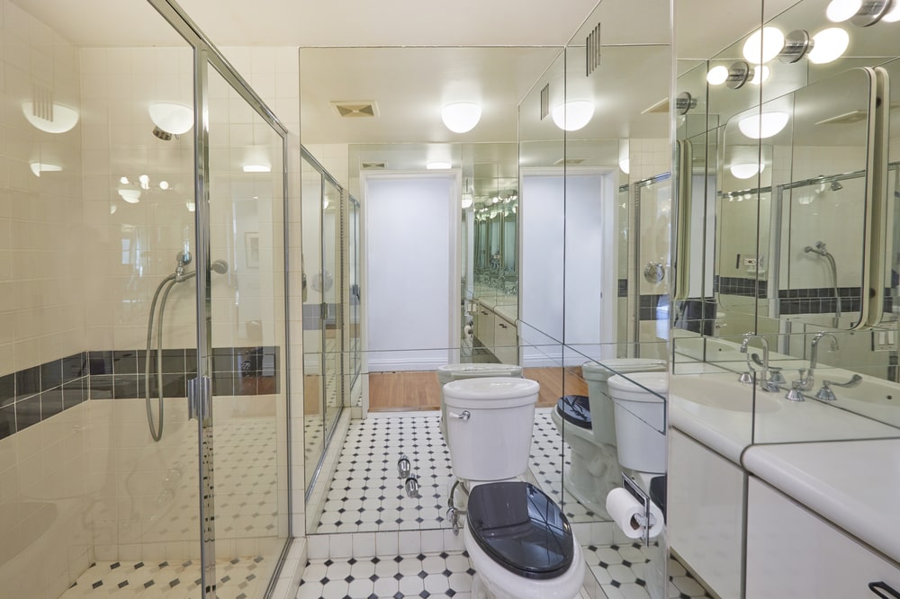 This bathroom has a glass-enclosed shower area across from the modern white vanity beside the toilet with a mirrored wall behind it. Image courtesy of Toptenrealestatedeals.com.