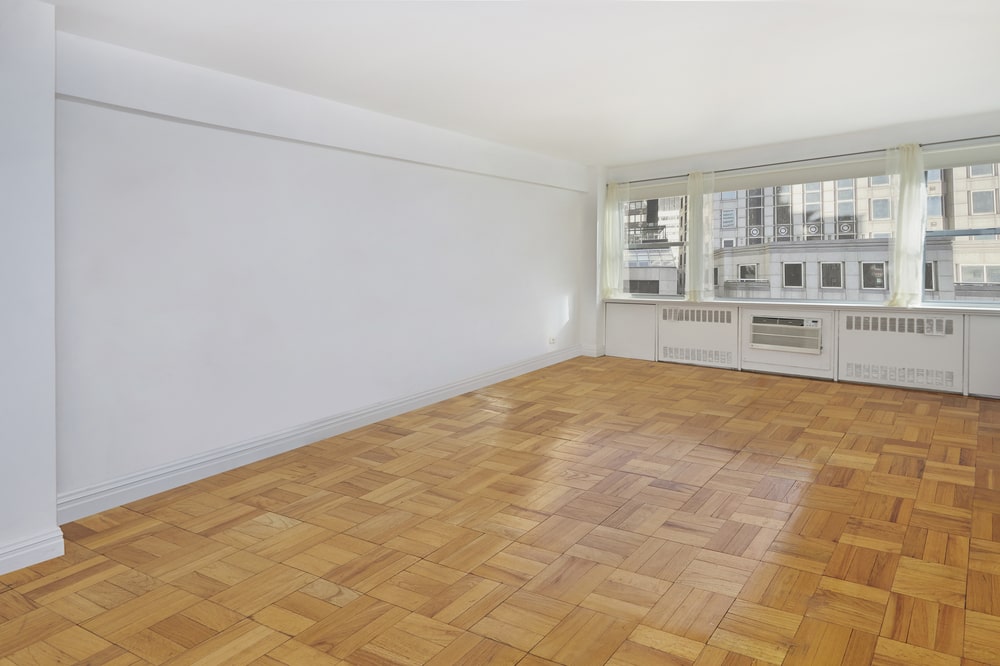 This is an empty bedroom with patterned hardwood flooring, white walls, white ceiling and a large window at the far end. Image courtesy of Toptenrealestatedeals.com.