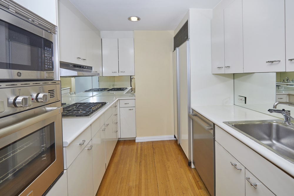 The long and narrow kitchen has white shaker cabinets lining the walls that make the stainless steel appliances stand out. Image courtesy of Toptenrealestatedeals.com.