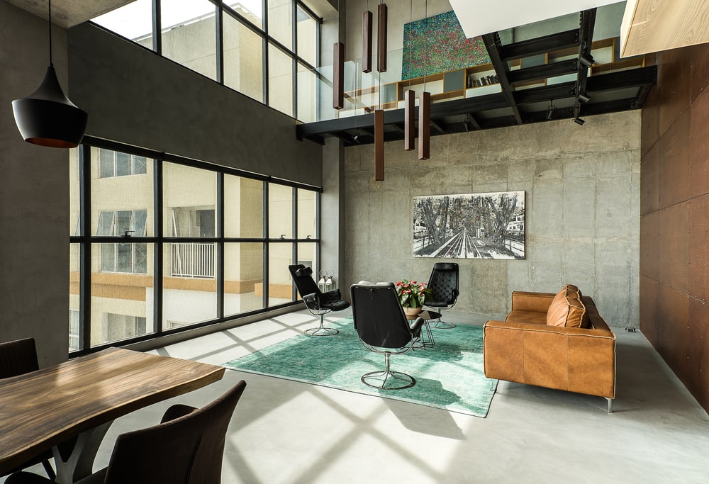 This is a full view of the living room that has a large brown leather sofa across from the large glass wall that brings in natural lighting.